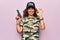 Middle age beautiful hunter woman wearing camouflage t-shirt and usa cap holding gun doing ok sign with fingers, smiling friendly