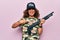 Middle age beautiful hunter woman wearing camouflage t-shirt and usa cap holding shotgun smiling happy pointing with hand and