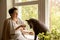 Middle age beautiful woman sitting on windowsill with her dog. 50-year-old woman spending time with her Mexican hairless