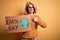 Middle age blonde woman asking for the enviroment holding banner with earth day message happy with big smile doing ok sign, thumb