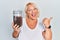 Middle age blonde woman holding raisins bowl pointing thumb up to the side smiling happy with open mouth