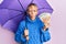 Middle age blonde woman holding umbrella and 50 euros banknotes sticking tongue out happy with funny expression