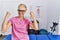 Middle age blonde woman at pain recovery clinic very happy and excited doing winner gesture with arms raised, smiling and