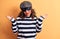 Middle age brunette burglar woman wearing mask and cap standing over yellow background clueless and confused with open arms, no