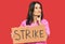 Middle age brunette doctor woman holding strike banner cardboard serious face thinking about question with hand on chin,