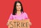 Middle age brunette doctor woman holding strike banner cardboard thinking attitude and sober expression looking self confident