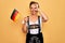 Middle age brunette patriotic woman wearing traditional octoberfest dress holding german flag with happy face smiling doing ok