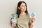 Middle age brunette woman holding charity jar with money and we need you paper smiling looking to the side and staring away