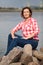 Middle age Caucasian woman portrait sitting on stones near water, looking at camera