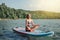 Middle age Caucasian woman sitting riding on paddle sup surfboard at sunset.