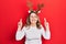 Middle age caucasian woman wearing cute christmas reindeer horns gesturing finger crossed smiling with hope and eyes closed