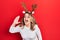 Middle age caucasian woman wearing cute christmas reindeer horns shouting and screaming loud to side with hand on mouth