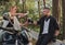 Middle age couple drinking tea, sitting on a motorcycle, traveling together on a forest road