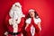Middle age couple wearing Santa costume and glasses over isolated red background begging and praying with hands together with hope