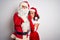 Middle age couple wearing Santa costume hugging over isolated white background hand on mouth telling secret rumor, whispering