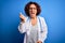 Middle age curly hair doctor woman wearing coat and stethoscope over blue background angry and mad raising fist frustrated and