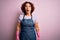 Middle age curly hair woman cleaning doing housework wearing apron and gloves afraid and shocked with surprise expression, fear