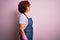 Middle age curly hair woman cleaning doing housework wearing apron and gloves looking to side, relax profile pose with natural