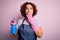 Middle age curly hair woman cleaning doing housework wearing apron and gloves using spayer cover mouth with hand shocked with