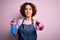 Middle age curly hair woman cleaning doing housework wearing apron and gloves using spayer pointing with finger to the camera and