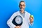 Middle age grey-haired man as nutritionist doctor holding weighing machine and green apple relaxed with serious expression on face