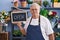 Middle age grey-haired man florist smiling confident holding open blackboard at florist