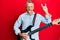 Middle age grey-haired man playing electric guitar doing rock sign sticking tongue out happy with funny expression