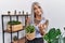 Middle age grey-haired woman holding green plant pot at home beckoning come here gesture with hand inviting welcoming happy and