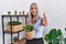 Middle age grey-haired woman holding green plant pot at home smiling friendly offering handshake as greeting and welcoming