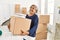 Middle age grey-haired woman smiling happy holding books cardboard box at new home