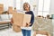 Middle age grey-haired woman smiling happy holding books cardboard box at new home