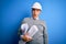 Middle age handsome grey-haired architect man wearing safety helmet holding blueprints In shock face, looking skeptical and