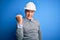 Middle age handsome grey-haired engineer man wearing safety helmet over blue background angry and mad raising fist frustrated and