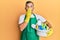 Middle age handsome man holding cleaning products covering mouth with hand, shocked and afraid for mistake