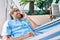 Middle age handsome man at the terrace of his house relaxing lying on a hammock speaking on the phone