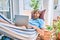 Middle age handsome man at the terrace of his house relaxing lying on a hammock working with laptop