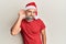 Middle age handsome man wearing christmas hat and summer t-shirt smiling with hand over ear listening and hearing to rumor or