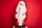 Middle age handsome man wearing Santa costume standing over isolated red background begging and praying with hands together with