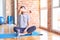 Middle age handsome sportman sitting on mat doing stretching yoga exercise at gym covering eyes with arm, looking serious and sad