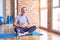 Middle age handsome sportman sitting on mat doing stretching yoga exercise at gym smiling and laughing hard out loud because funny