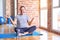 Middle age handsome sportman sitting on mat doing stretching yoga exercise at gym smiling showing both hands open palms,