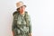 Middle age hiker woman wearing backpack canteen hat glasses over isolated white background smiling looking to the side and staring