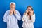 Middle age hispanic couple standing over blue background rubbing eyes for fatigue and headache, sleepy and tired expression