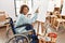 Middle age hispanic disabled artist woman drawing sitting on wheelchair at art studio