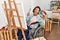 Middle age hispanic disabled artist woman drawing sitting on wheelchair at art studio