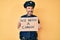 Middle age hispanic man wearing police uniform holding we need a change banner smiling looking to the side and staring away