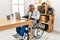 Middle age hispanic man working at the office sitting on wheelchair with sad expression covering face with hands while crying