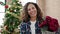 Middle age hispanic woman holding christmas plant at home