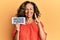 Middle age hispanic woman holding hedge funds message paper smiling with an idea or question pointing finger with happy face,