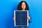 Middle age hispanic woman holding photovoltaic solar panel puffing cheeks with funny face